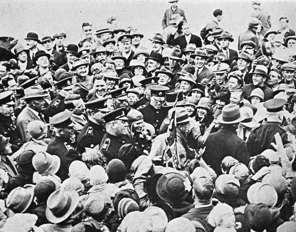Photo wide overhead shot of Earhart in flight                 gear escorted by police through a crowd